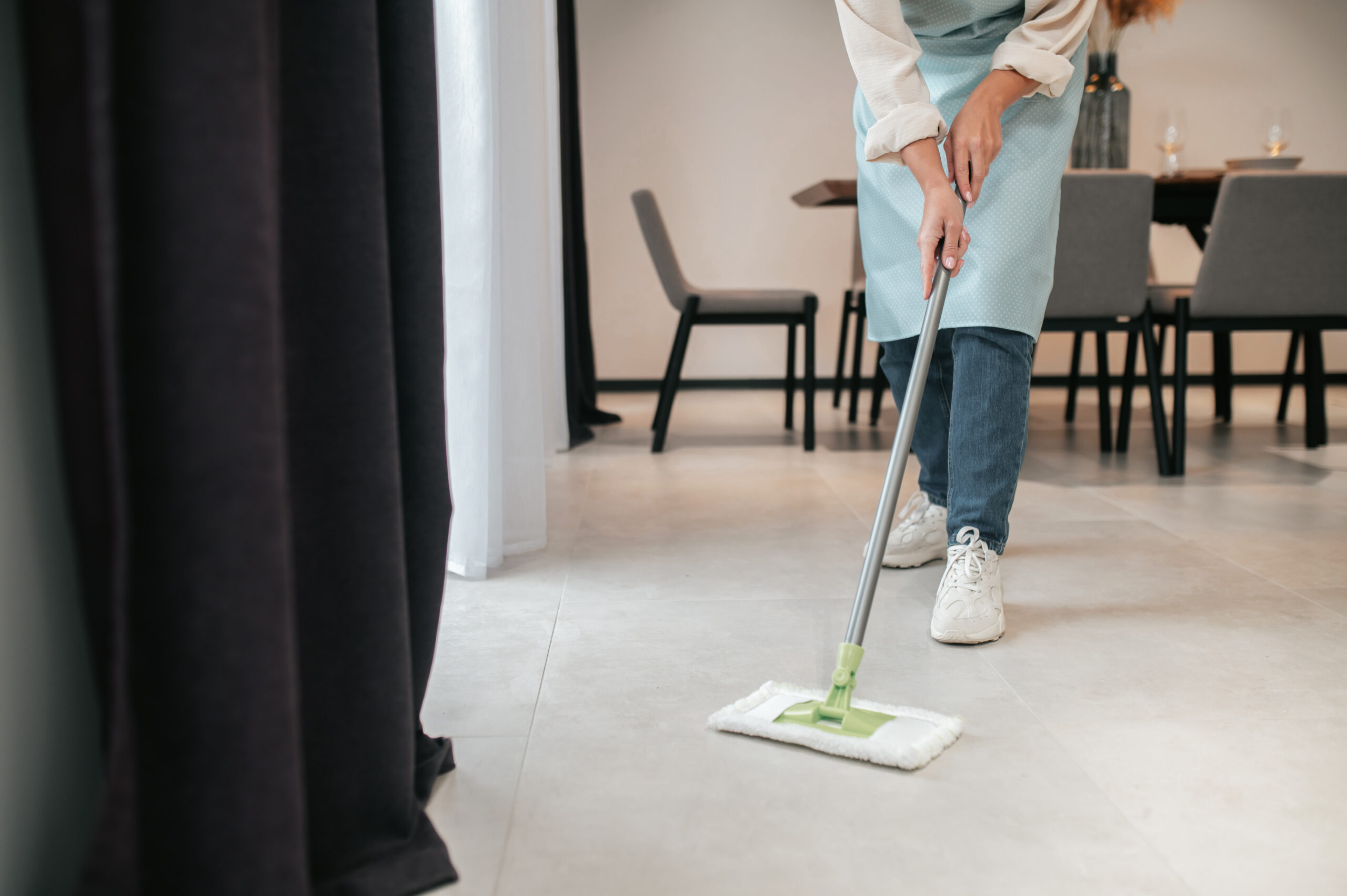Une femme qui nettoie un sol avec une mop, en tenue professionnelle dans un restaurant.